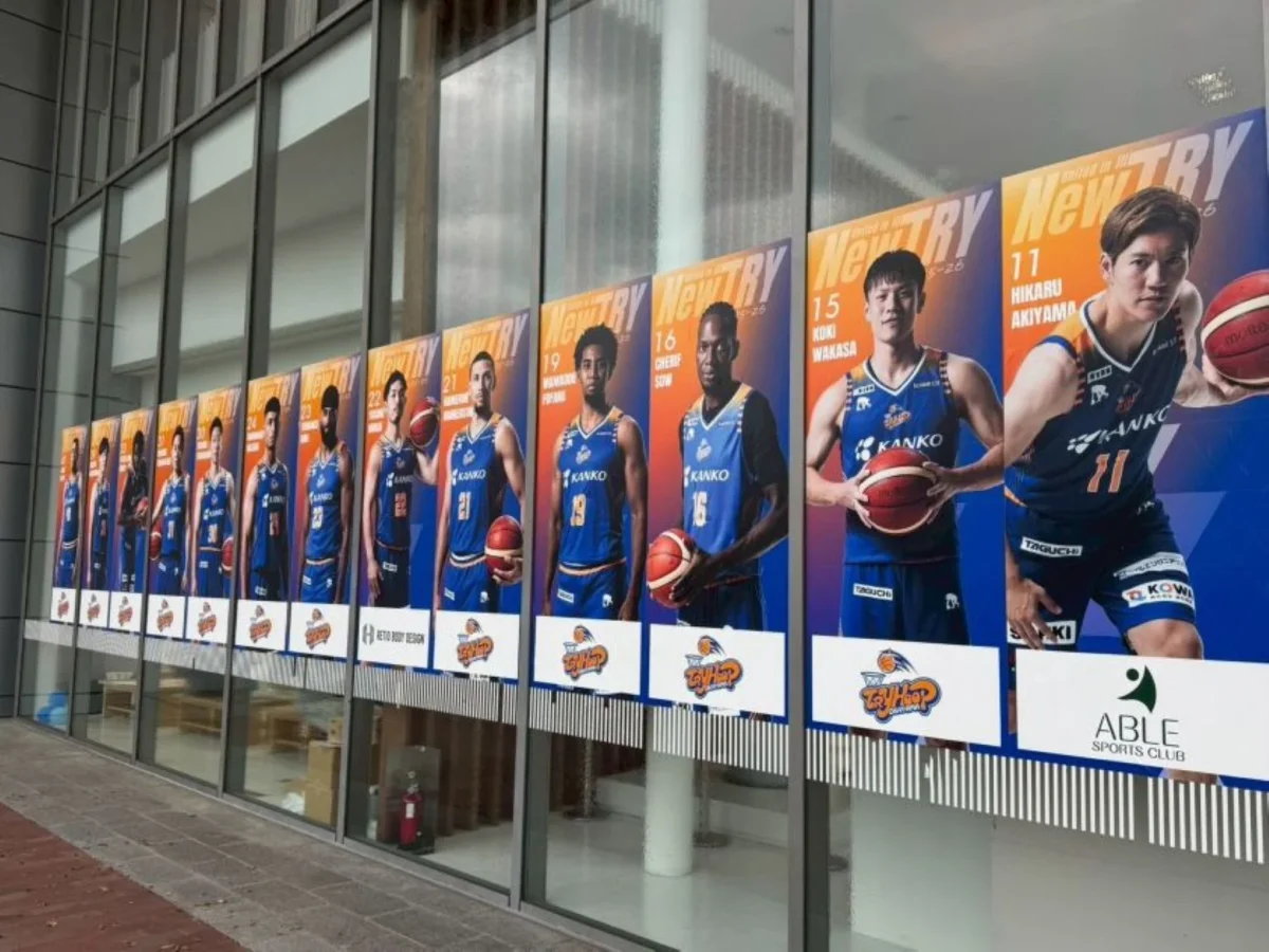 バスケットボールチームの選手写真を並べた大型ウィンドウ装飾の設置事例。選手ビジュアルを活用して施設のガラス面を装飾。