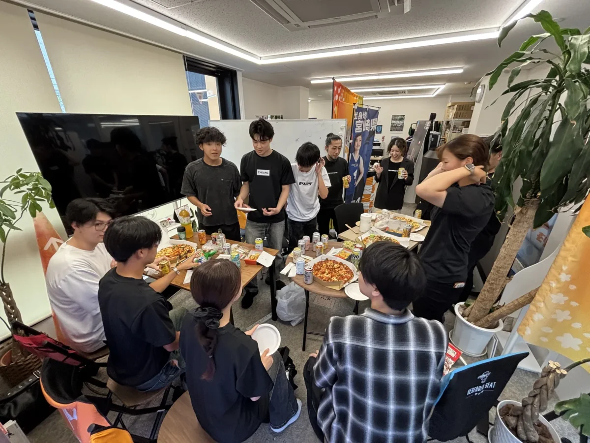オフィスで社員が飲み物を手に交流する社内懇親会の様子。