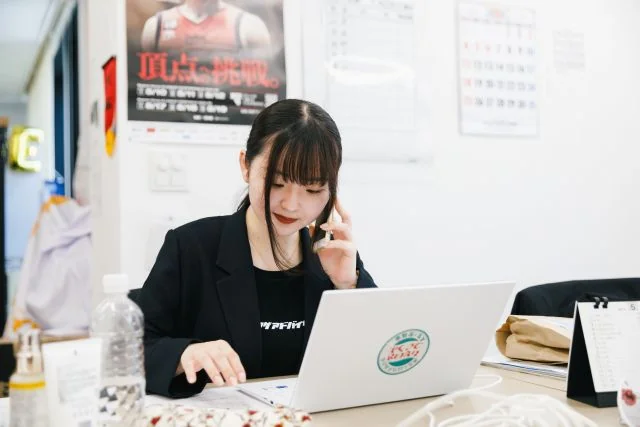 オフィスで電話対応をしながらノートパソコンを使って業務に取り組む社員の様子。