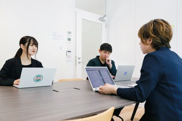 会議室でノートパソコンを使用しながら3名の社員が打ち合わせを行う様子。
