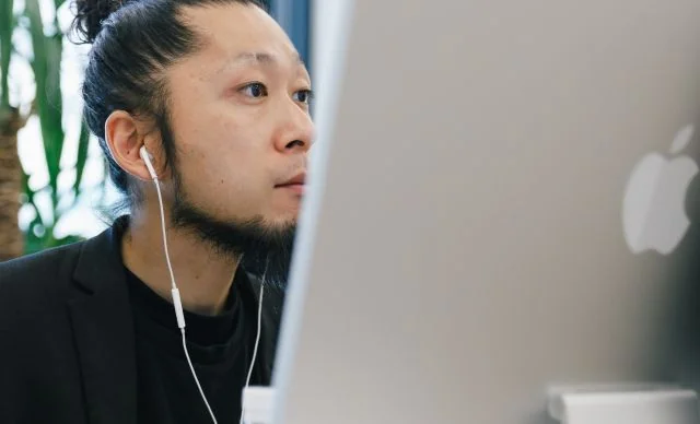 オフィスでイヤホンを着け、デスクトップパソコンを使って業務に取り組む社員の様子。
