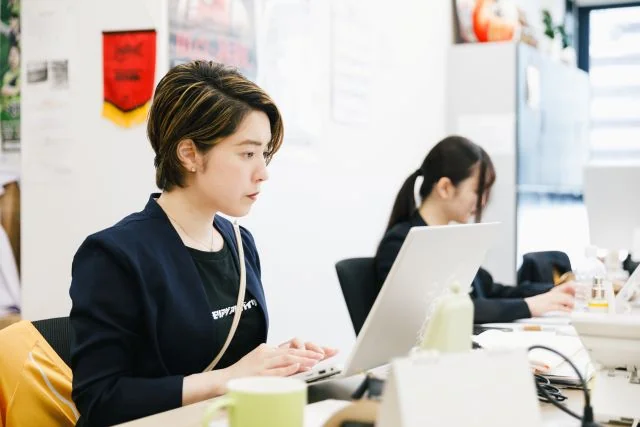 オフィスのデスクでノートパソコンを使って業務に取り組む社員の様子。