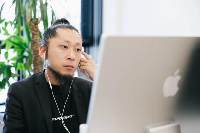 オフィスでイヤホンを着け、パソコンを使って業務に取り組む社員の様子。